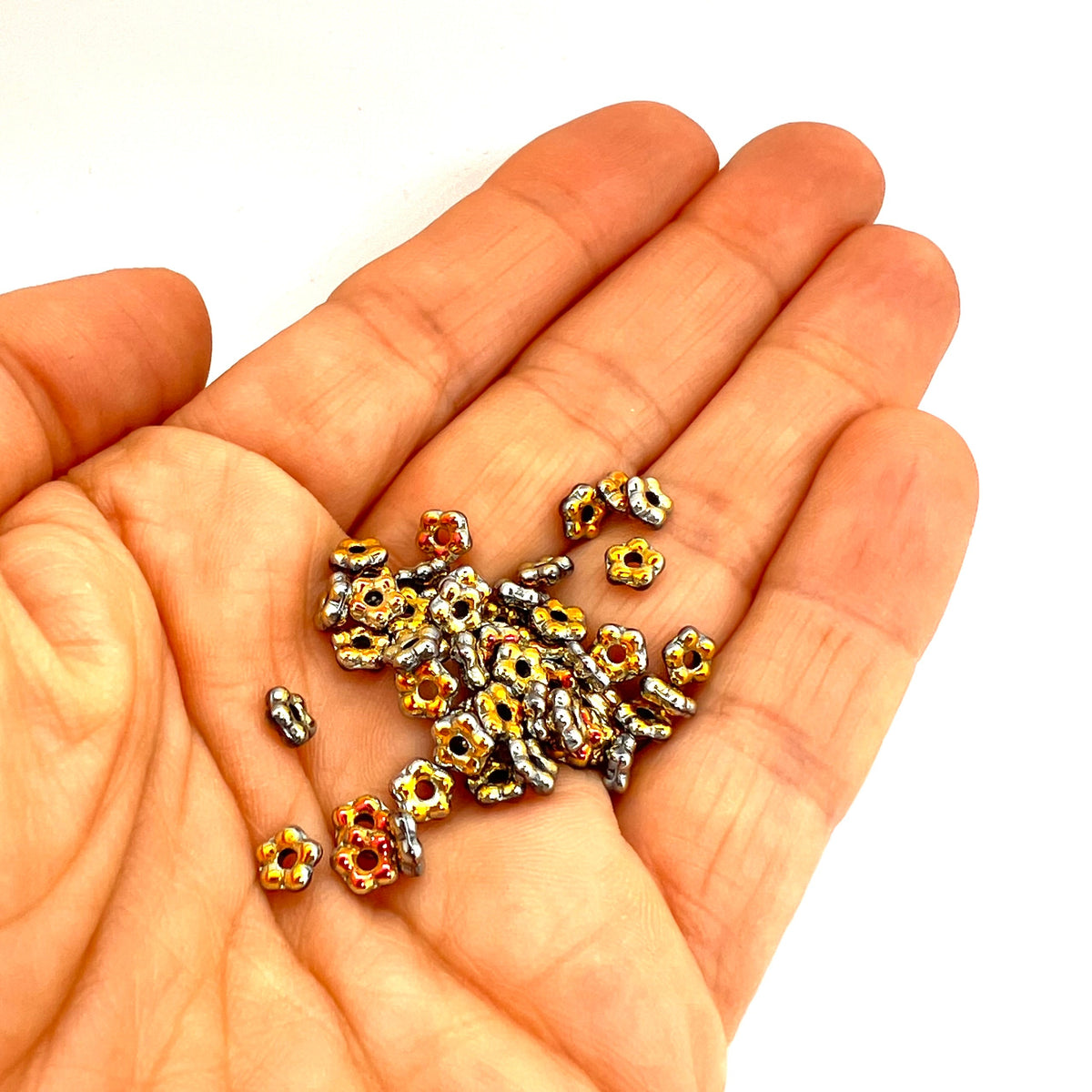 Hand holding small metallic flower beads on a white background