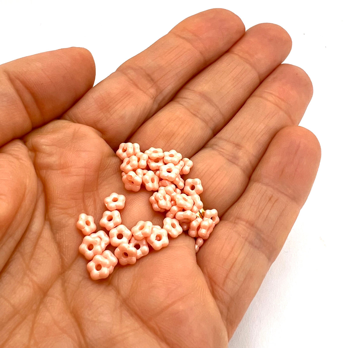 Hand holding small pink flower beads against a white background