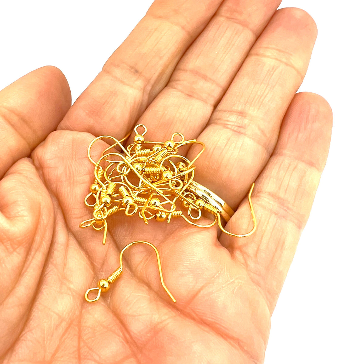 Gold earring hooks on a hand with a white background