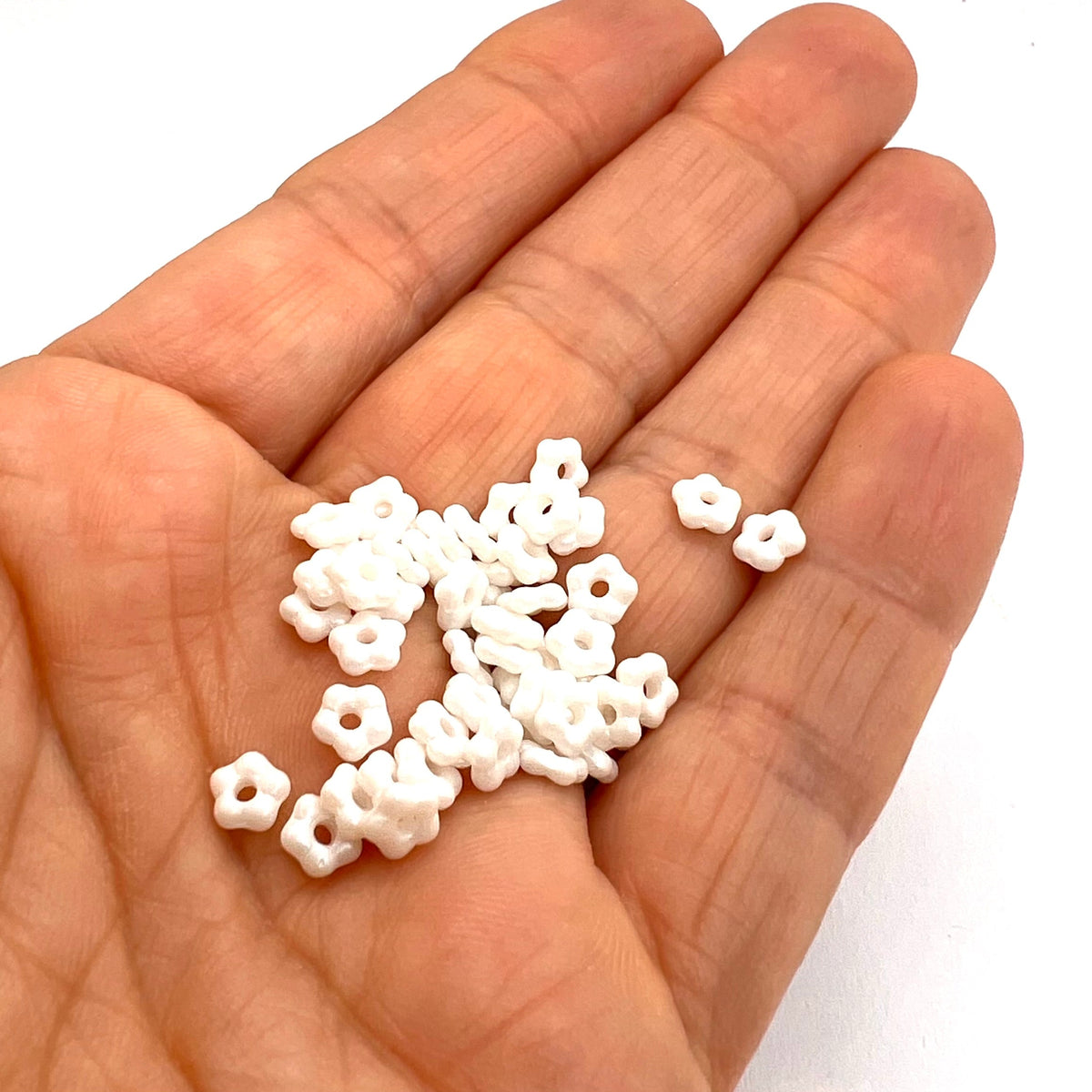 Hand holding small white flower beads against a white background